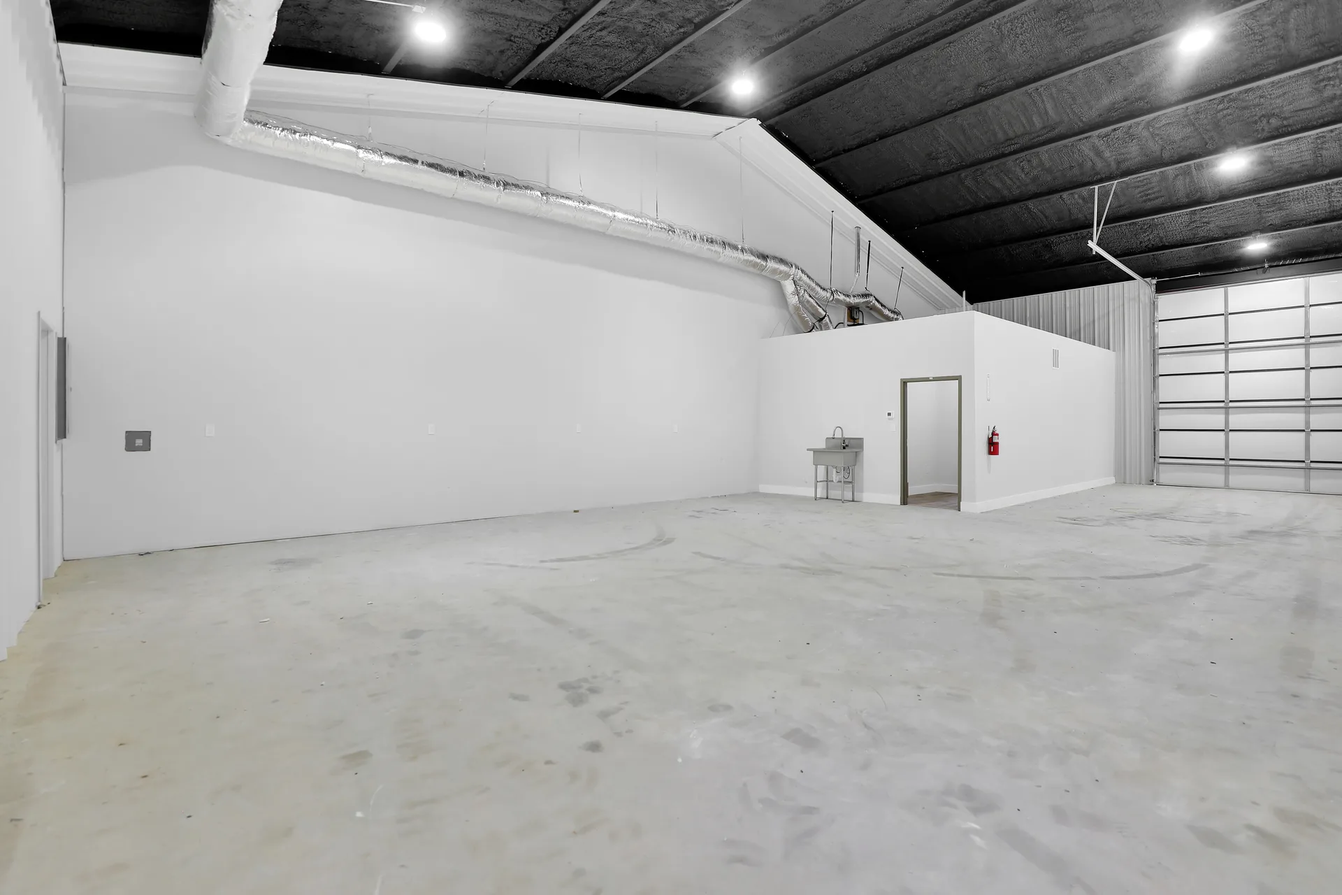 High-clearance warehouse area with overhead door, white partition wall, concrete floor, and fire extinguisher